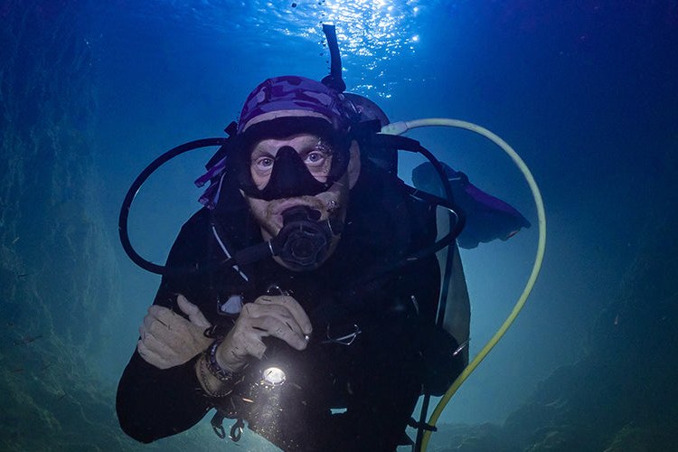 Diver underwater with a yellow low pressure inflator hose and a black regulator hose routed over the shoulder