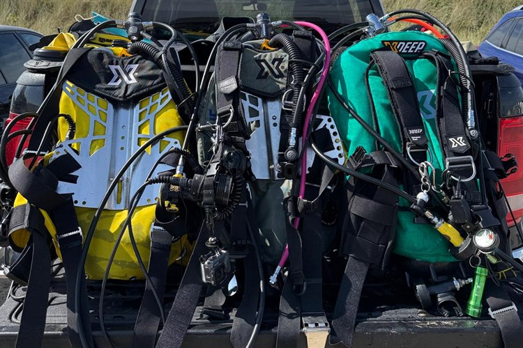 Three XDEEP backplate and wing systems rigged with regulators, ready on a tailgate before a dive